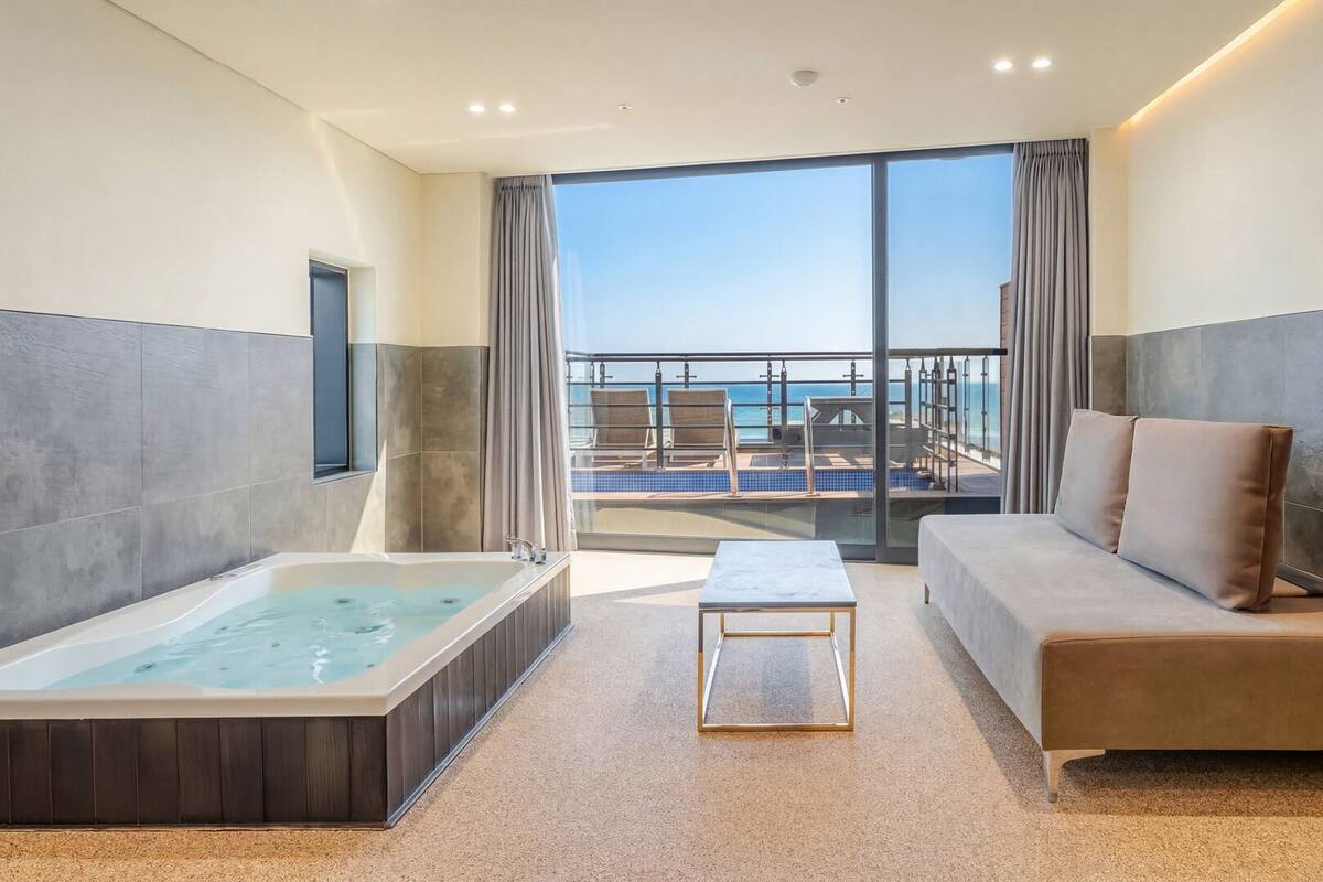 A modern hotel room with a large bathtub, a sofa, and a view of the ocean.