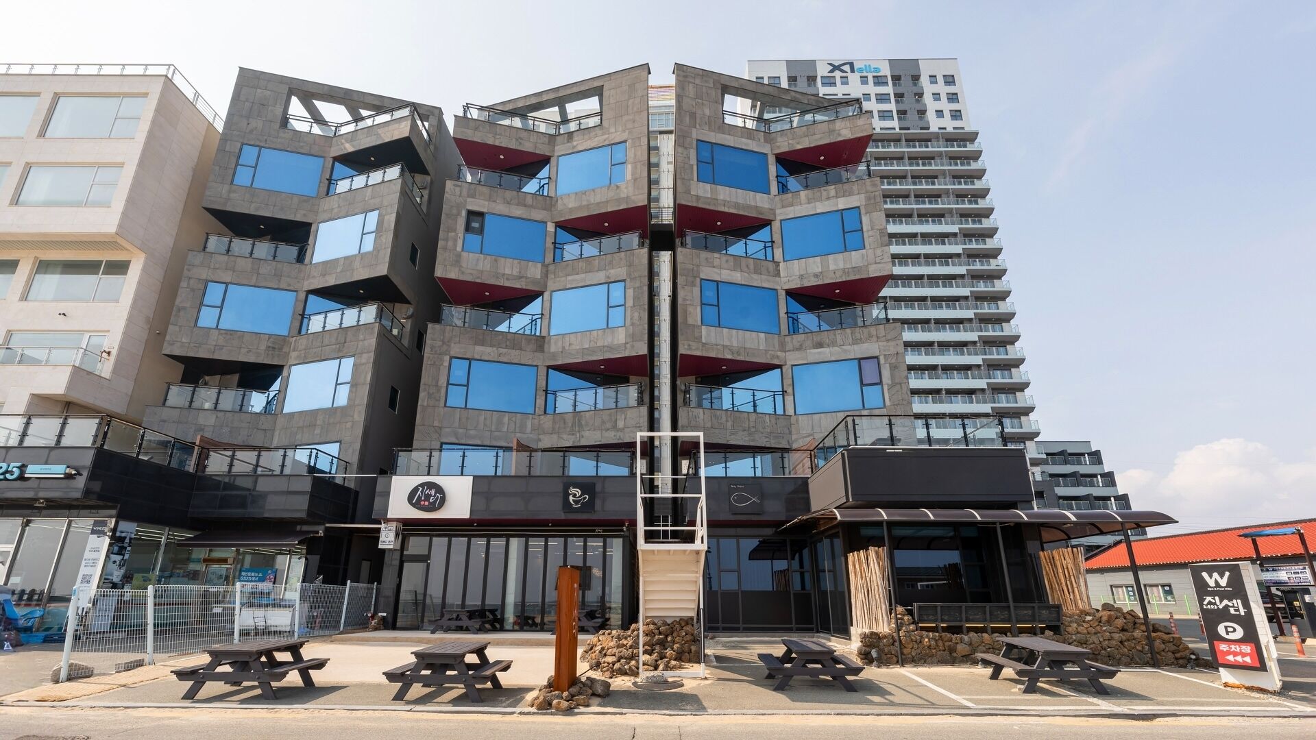 A modern multi-story building with balconies, a visible restaurant sign, and outdoor seating.