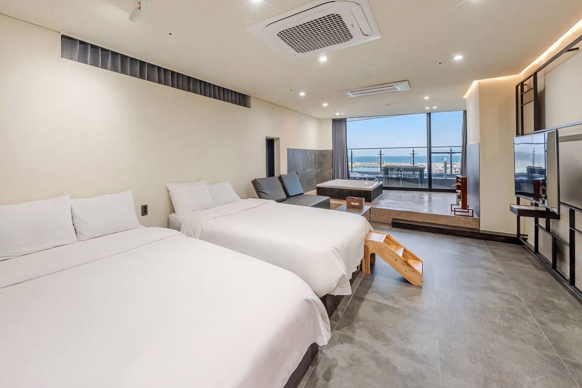 A hotel room with two beds, a large window with a view, a TV, and a balcony.