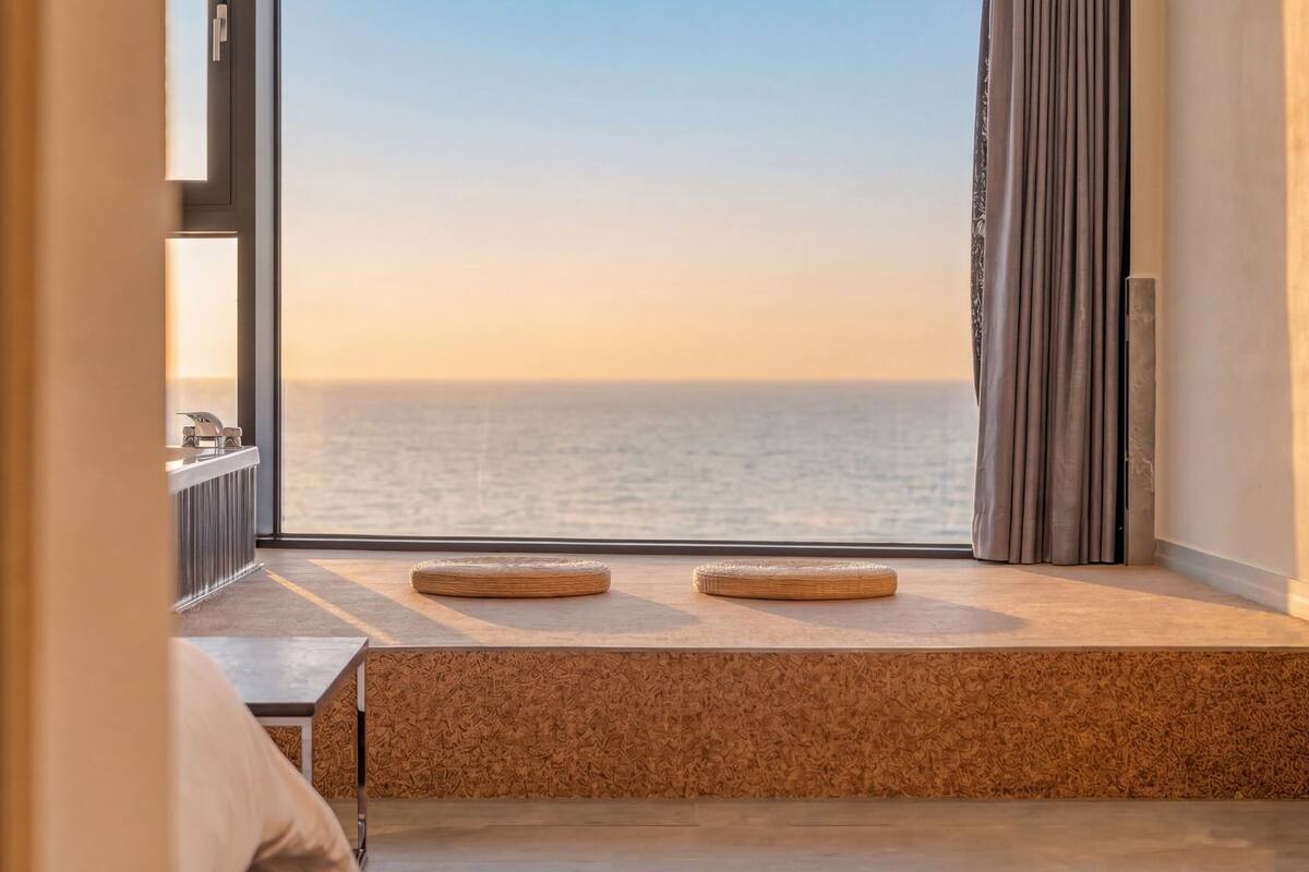 A room with a large window overlooking the sea, a wooden bench, and a radiator.