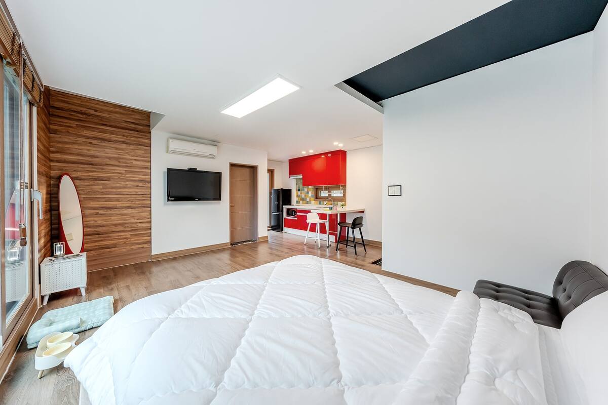 Ein modernes Hotelzimmer mit einem großen Bett, einer kleinen Küchenzeile und einem Fernseher.