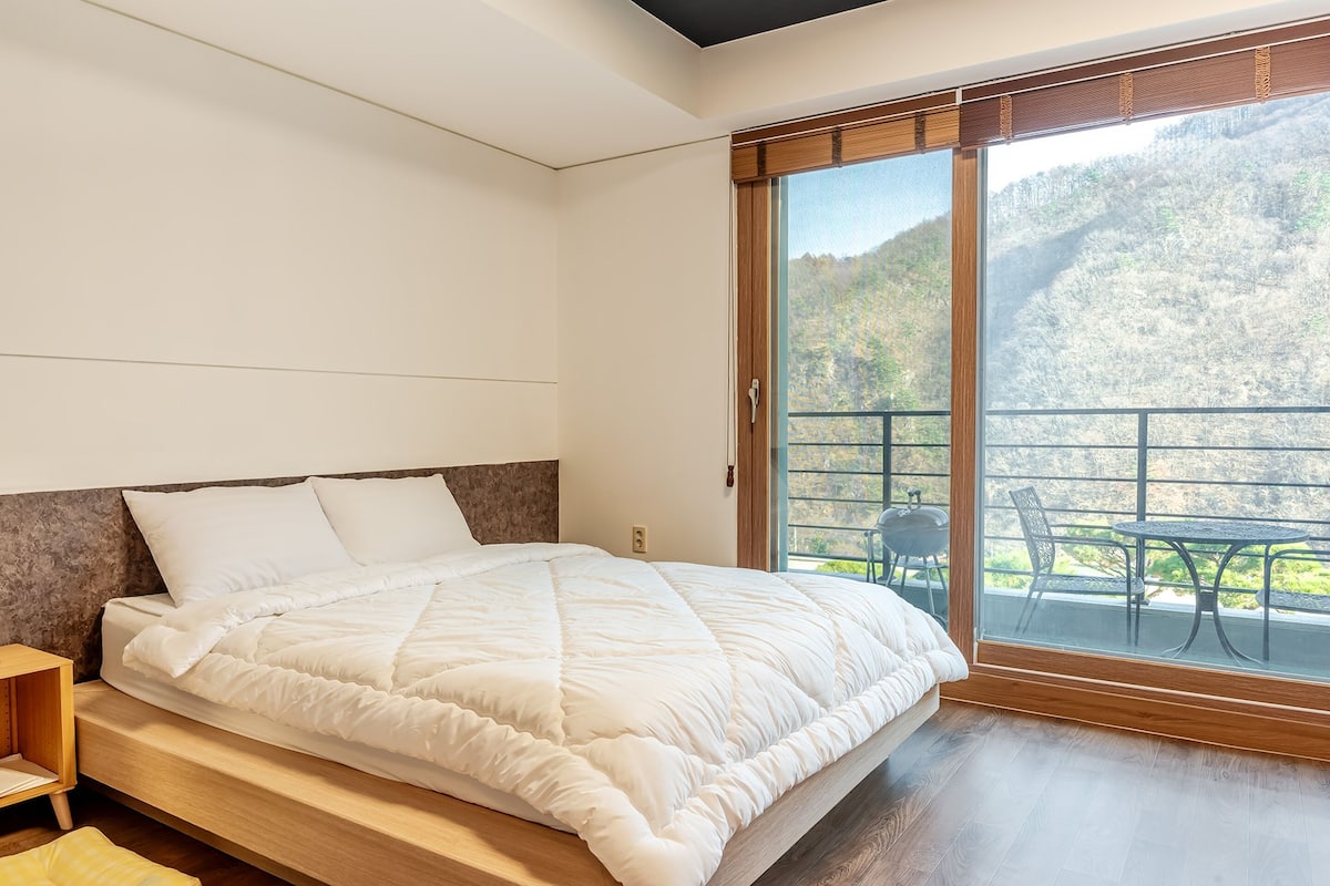 Ein Schlafzimmer mit einem großen Bett, einem Holzkopfende und Blick auf einen Balkon mit Sitzmöbeln.