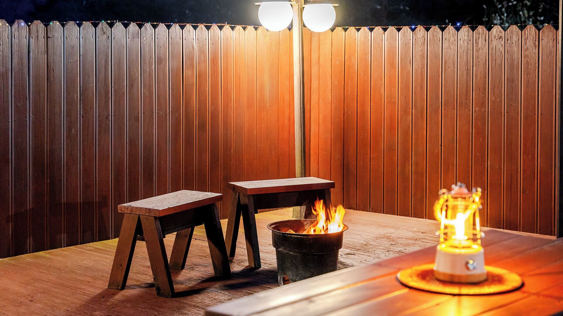 Una terraza de madera con un brasero de metal y dos taburetes de madera.