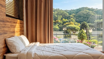 Un dormitorio con una cama grande, cabecero de madera y vistas a un balcón con plantas y árboles.