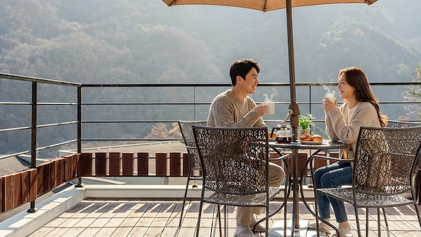 A couple seated at an outdoor table with a view of a mountainous landscape. - Gapyeong Meongstay Pension (Gapyeong)