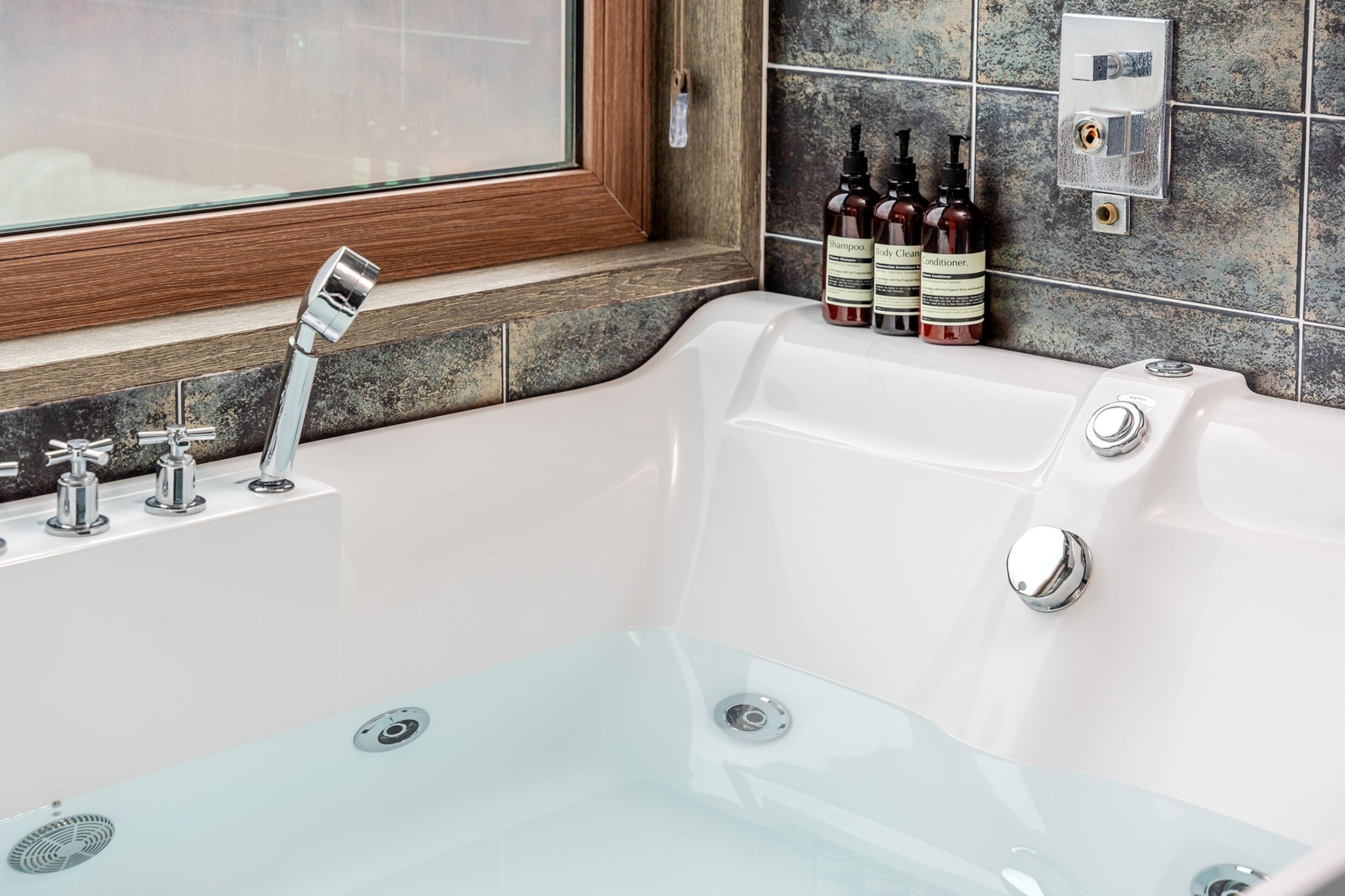 Une salle de bain moderne avec une baignoire entourée de parois en verre, des robinetteries chromées et un mur carrelé avec une fenêtre au-dessus du lavabo.