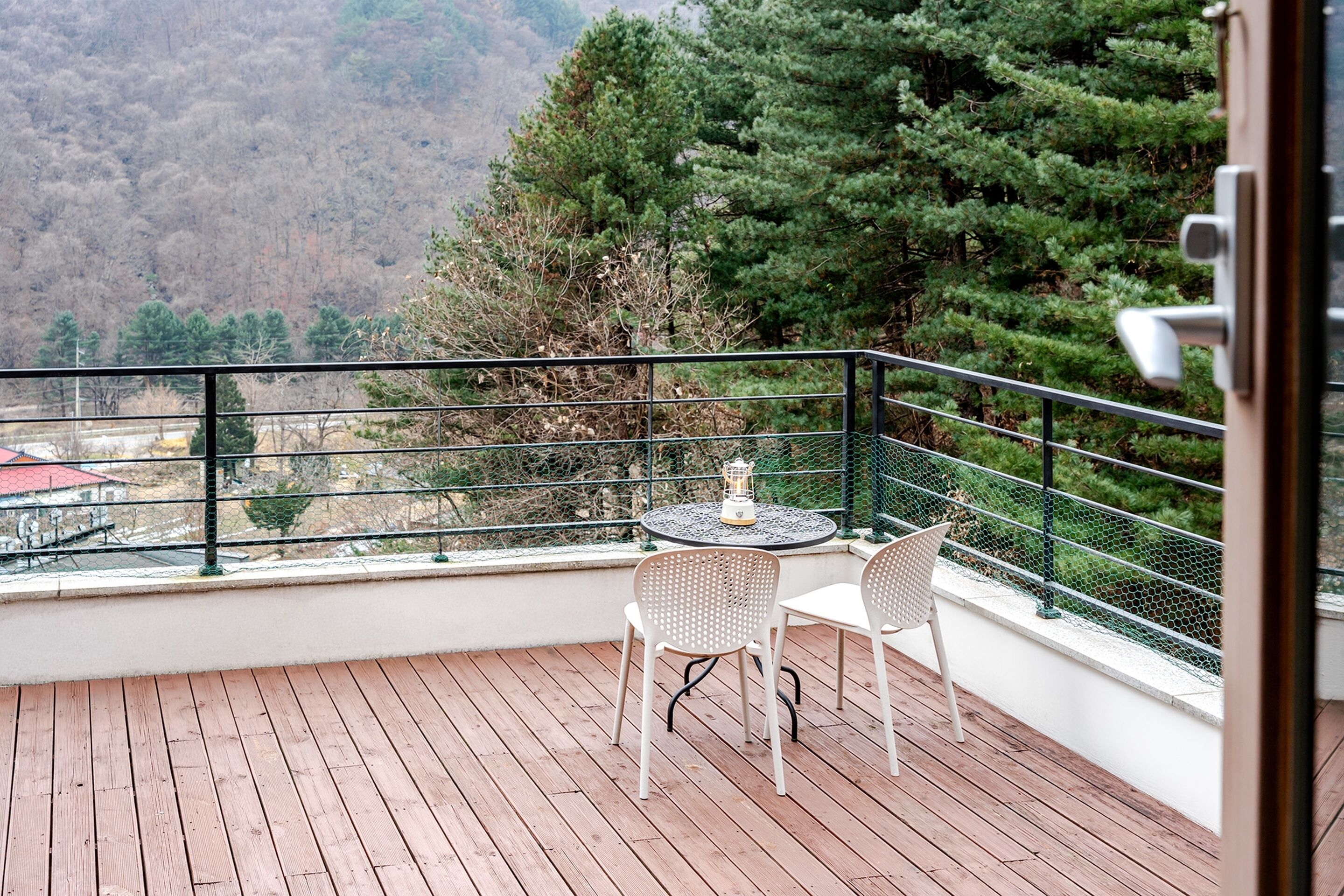 Un balcon doté d’un plancher en bois, de deux chaises blanches et d’une table sur laquelle est posée une lanterne.