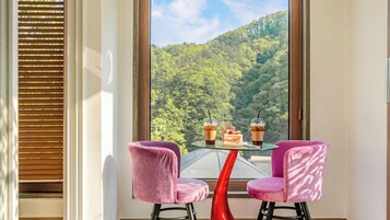 Una habitación con una mesa y dos sillas, una ventana que da a un bosque y una puerta con marco de madera.