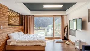 A modern bedroom with a wooden headboard, a large bed, a TV mounted on the wall, and a sliding glass door leading to a balcony. - Gapyeong Meongstay Pension (Gapyeong)