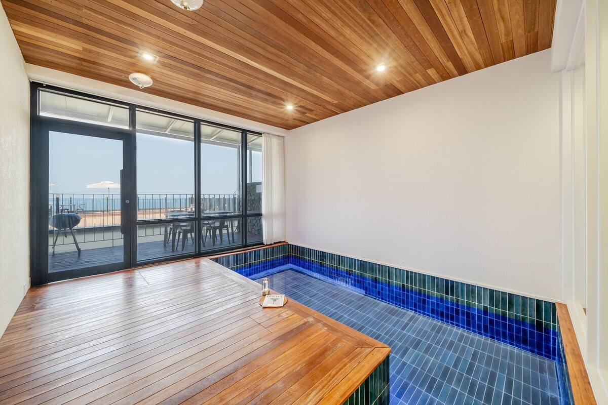 A room with a wooden ceiling, a large sliding glass door leading to a balcony, and a small pool area with blue tiles.