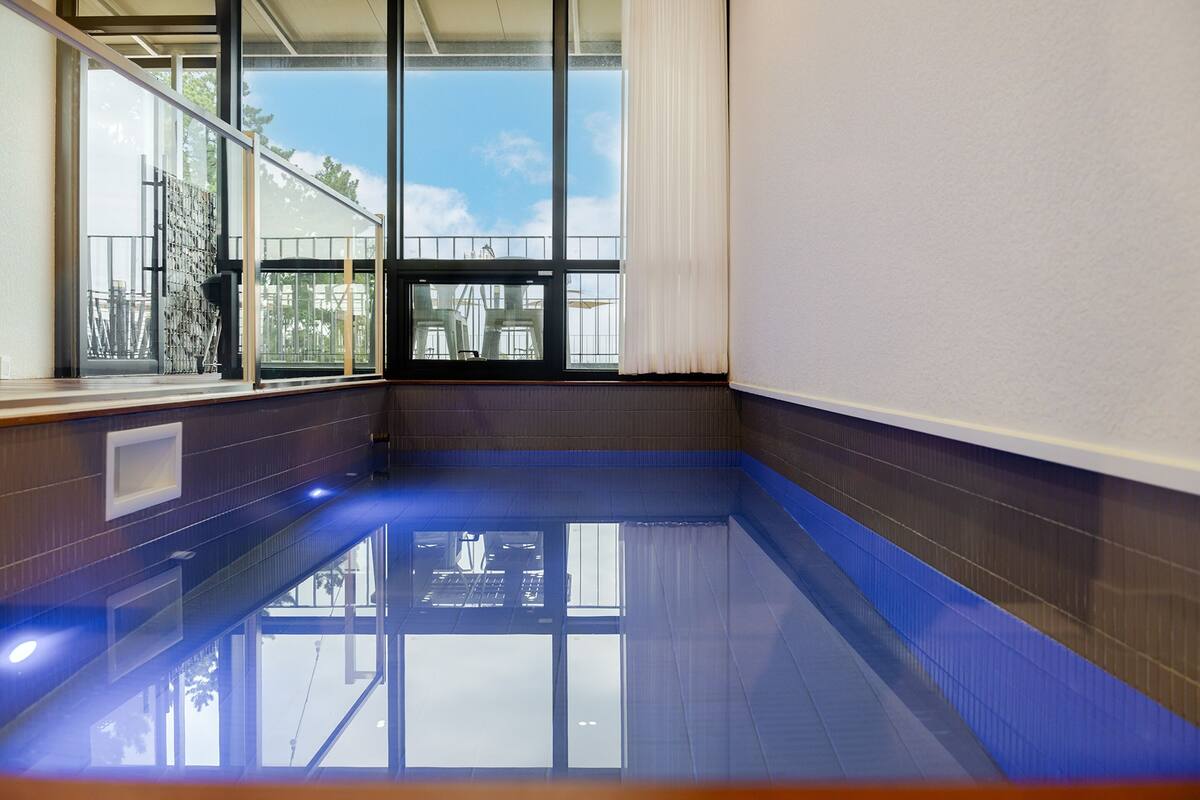 A swimming pool with clear glass walls, a view of the outdoors, and a window with a curtain.