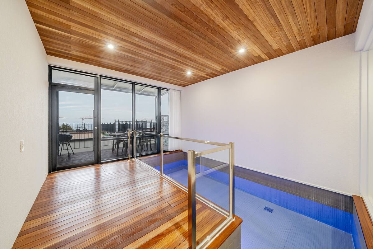 A modern interior with a wooden ceiling, large sliding glass doors leading to an outdoor area, and a small indoor pool.