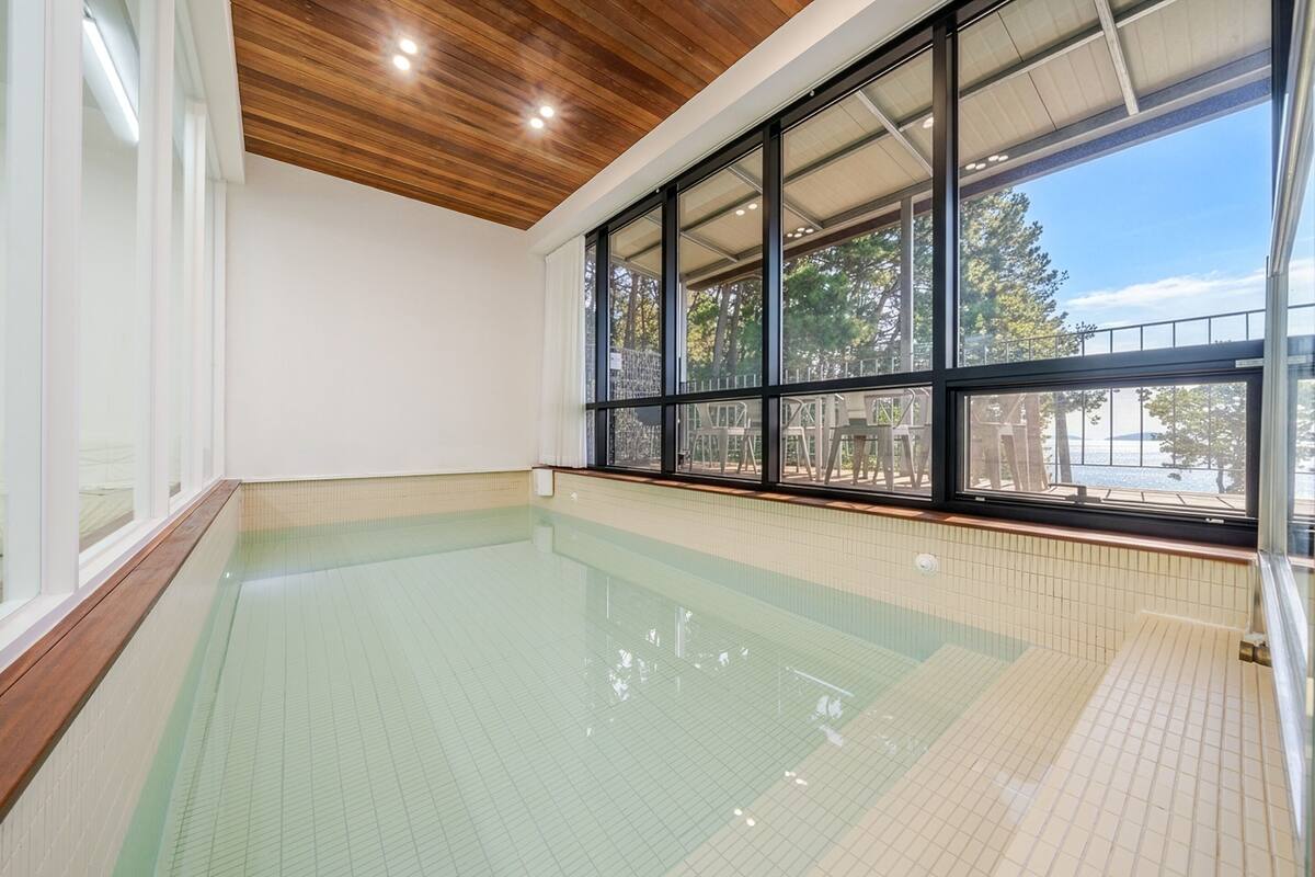 An indoor swimming pool with clear glass walls, wooden ceiling, and tiled floor.