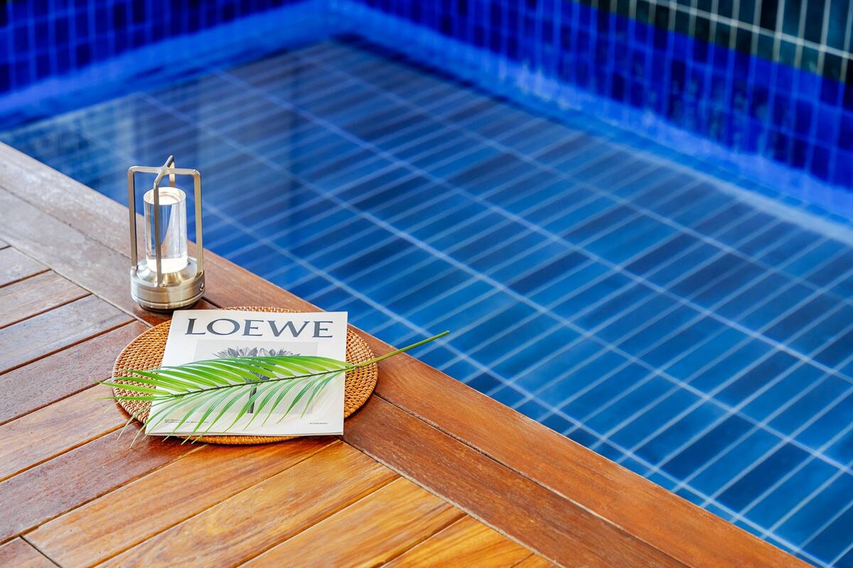 A wooden deck with a glass table, a candle, a magazine, and a palm leaf.