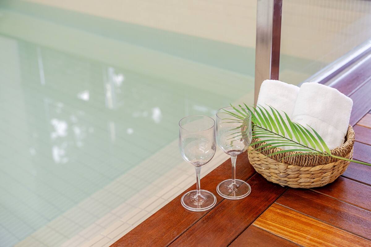 A wooden table with two clear glasses and a woven basket containing a white towel and a green palm leaf.