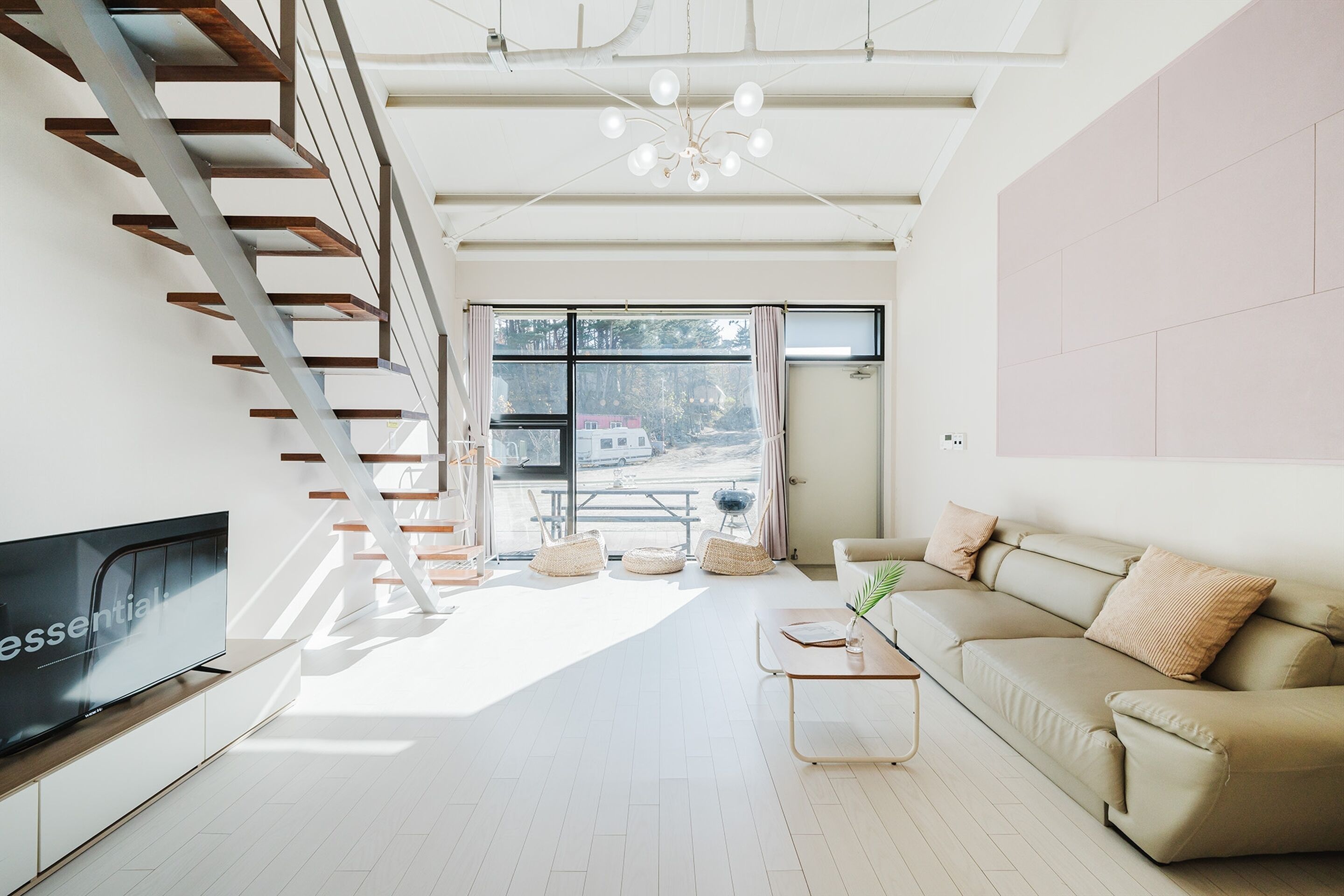 A modern living room with a flat-screen TV, a sofa, a coffee table, and a staircase.