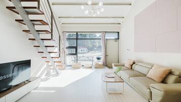 A modern living room with a flat-screen TV, a sofa, a coffee table, and a staircase.