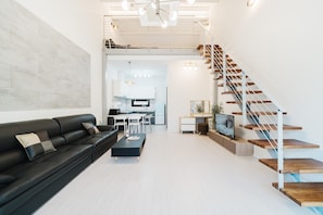 Una sala de estar moderna con un sofá de cuero negro, una mesa de centro y una escalera de madera.