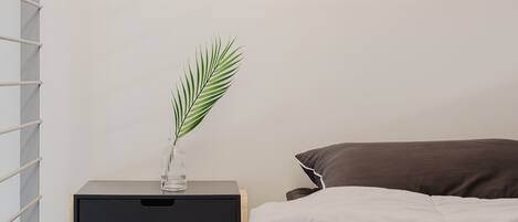 A bedroom with a bed, a bedside table with a plant, and a nightstand.