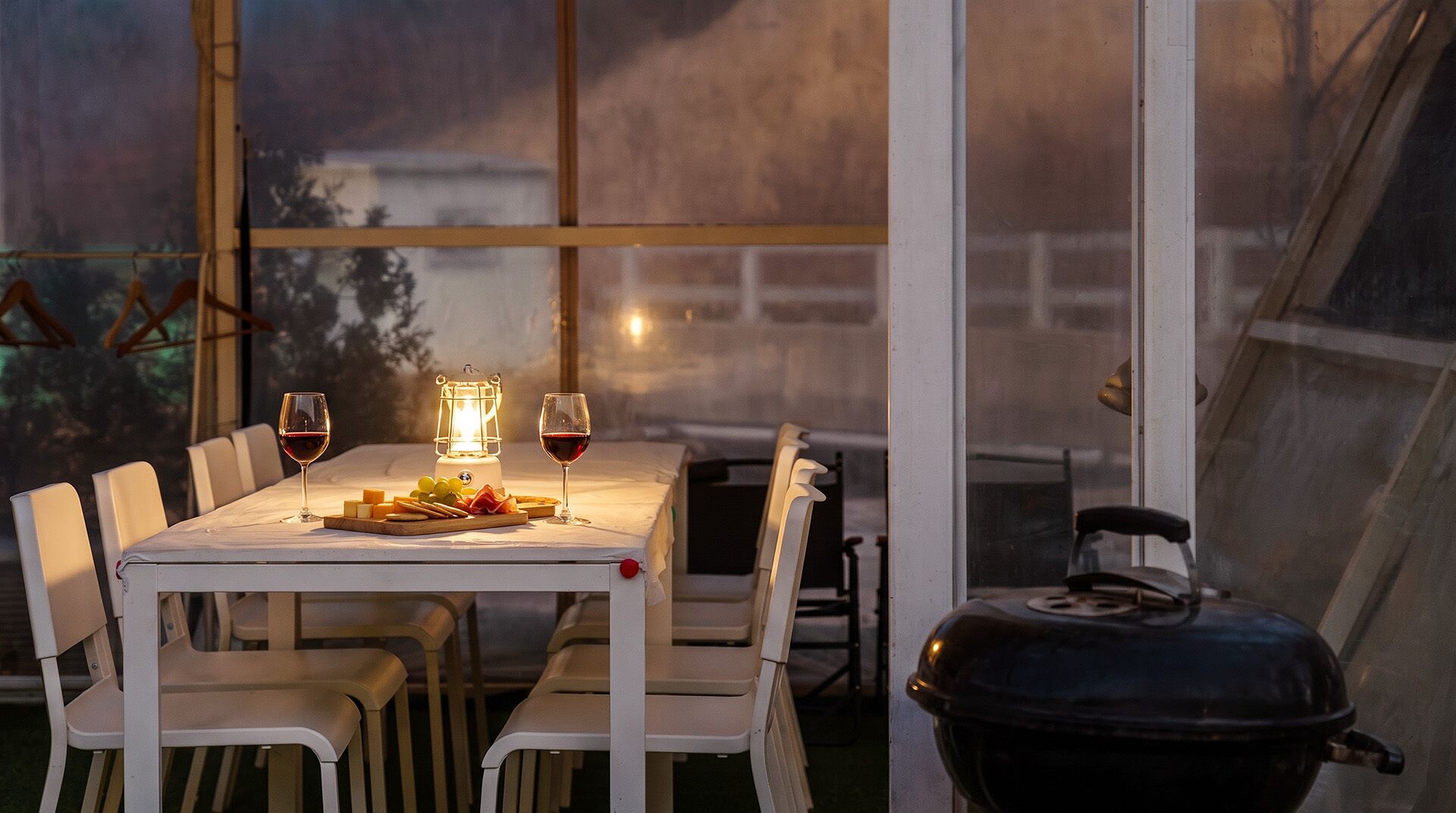 An outdoor dining area with a table set for two, a grill, and a lantern providing light.