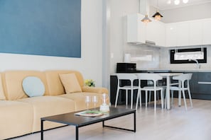Ein modernes Wohnzimmer mit einer Couch, einem Couchtisch und einer Küchenzeile mit weißen Schränken sowie einem Esstisch mit Stühlen.