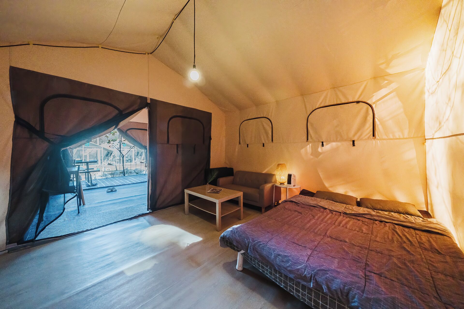A tent-style room with a bed, a small table, a sofa, and a lamp.