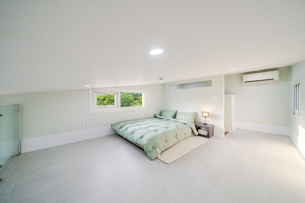 A bedroom with a bed, a nightstand, a window, and an air conditioning unit.