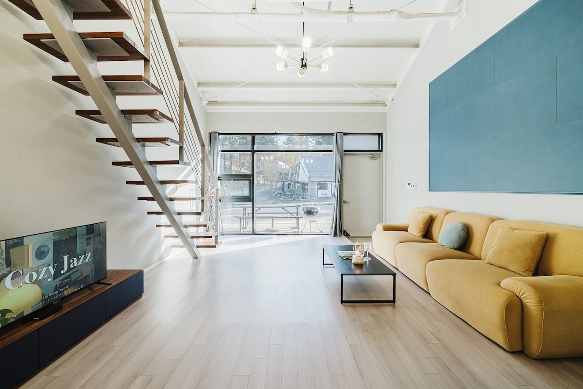 Un salon moderne avec un escalier, un canapé, une table basse et un téléviseur.