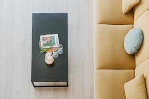 Una sala de estar moderna con una mesa de centro negra, un sofá color beige y una almohada azul claro, y un cuadro enmarcado sobre la mesa.