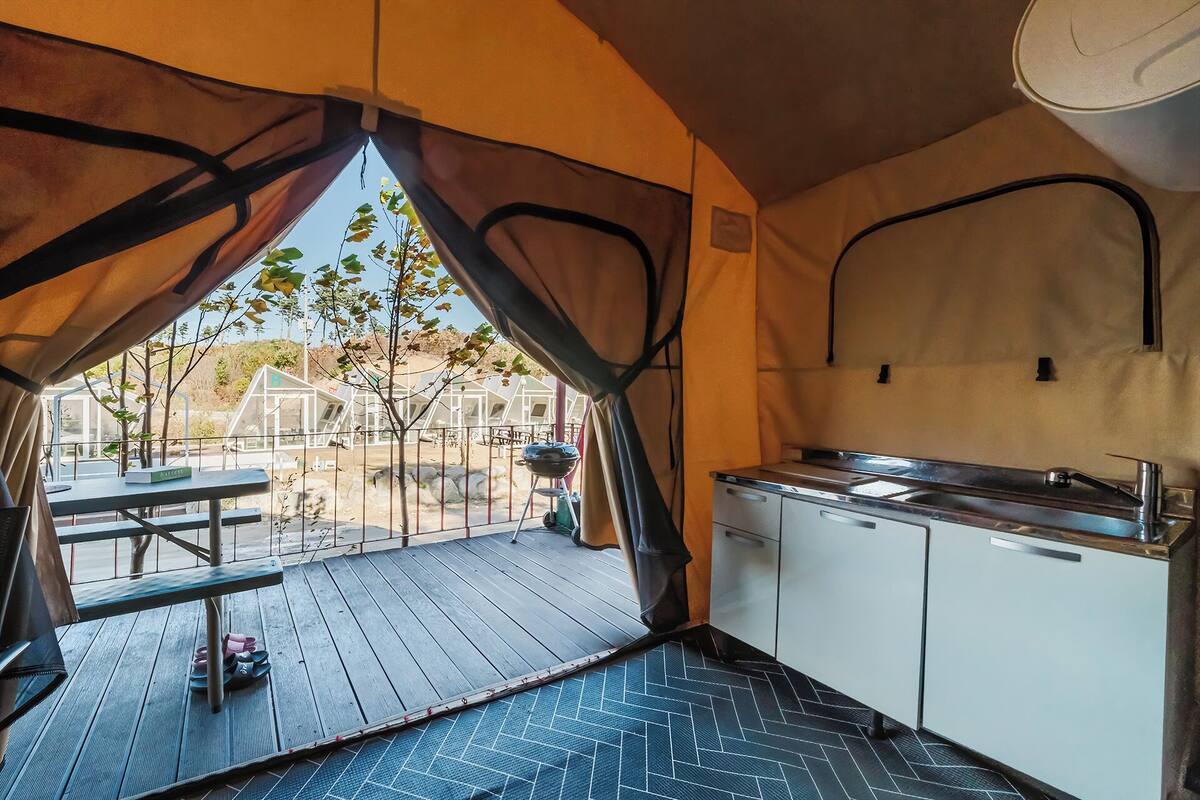 Une cuisine compacte avec un évier et des placards, une table à manger à l’extérieur, et une vue sur un espace clos planté d’arbres.