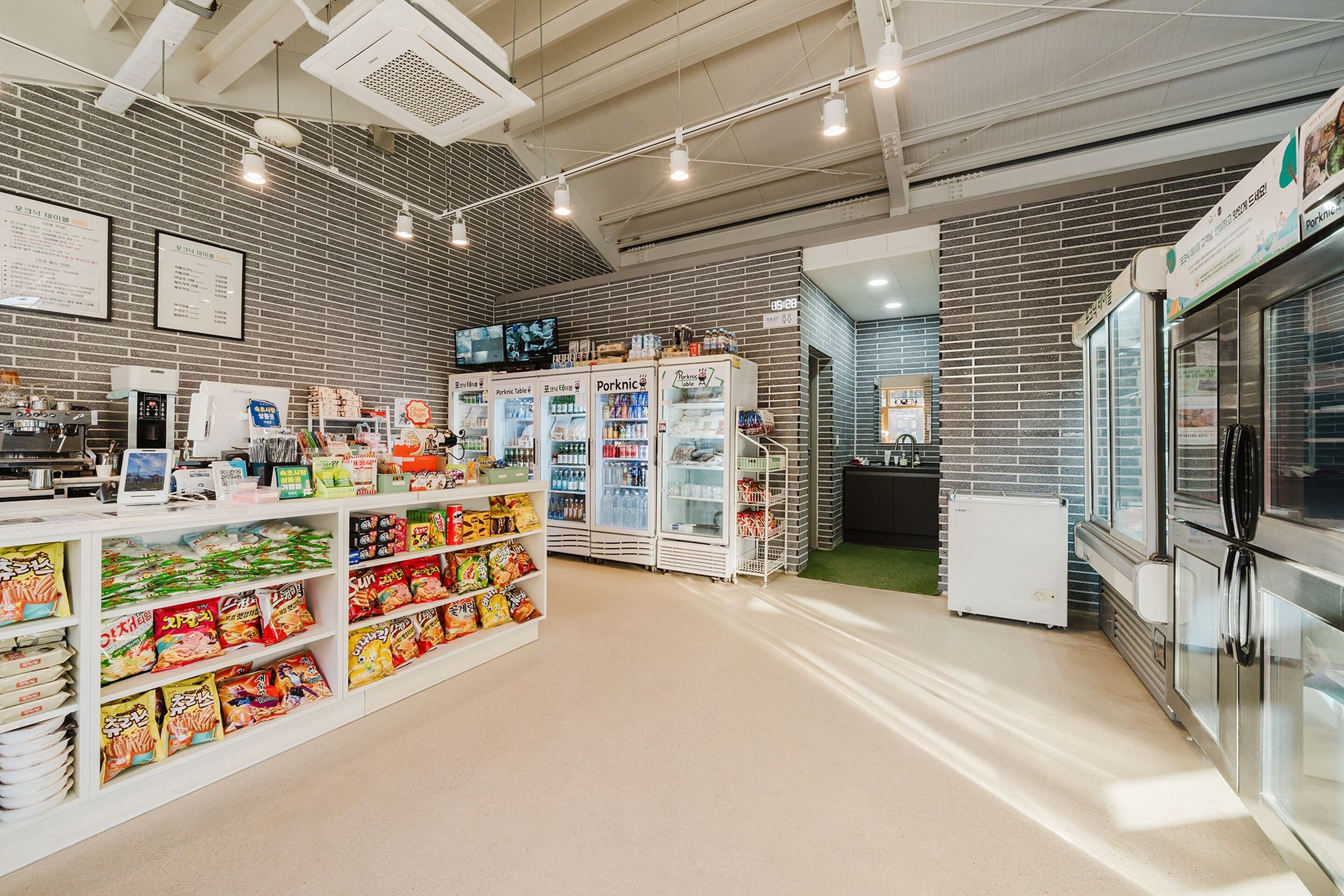 Una tienda moderna con pared de ladrillo, vitrinas refrigeradas y una variedad de productos envasados en estanterías.
