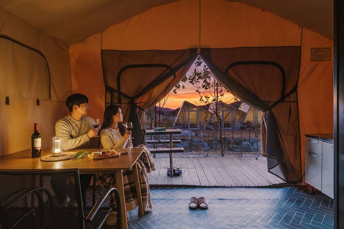 Un espace de restauration aménagé sous une tente, avec une table dressée pour deux personnes, une bouteille de vin et une bougie.