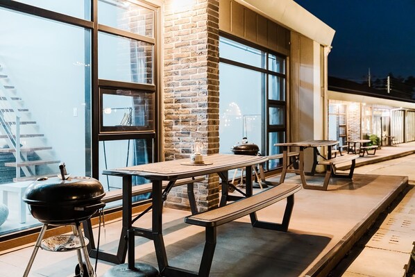 An outdoor patio area with wooden tables and benches, a grill, and a brick wall. - Sokcho Starry Night Glamping (Sokcho)