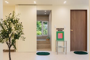 Un couloir avec une porte en bois, une plante verte, un escalier et un panneau indiquant « MODE CRÉATIVE ».