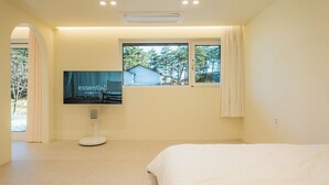 Een slaapkamer met een bed, een aan de muur bevestigde televisie en een raam met gordijnen.