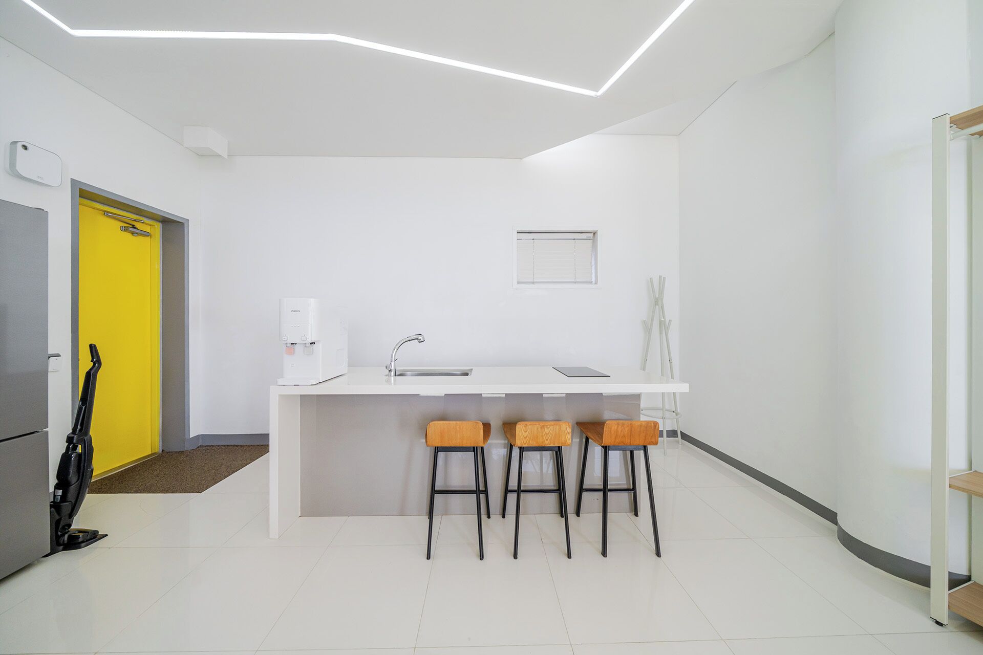 A modern kitchen with a white countertop, a built-in sink, and three bar stools.