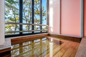 A room with a wooden floor, large windows with a view of trees, and a pink wall.