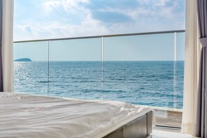 Une chambre avec un lit et une vue sur la mer, visible à travers une fenêtre en verre.