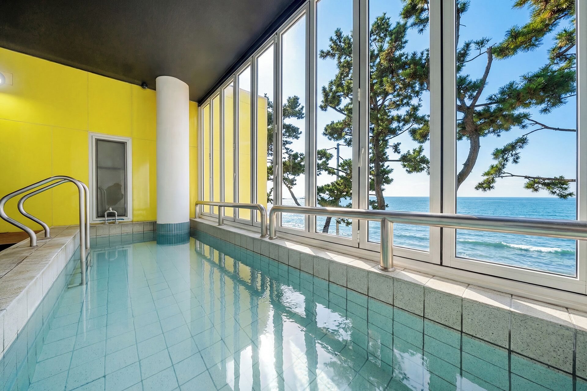 An indoor swimming pool with a view of the sea through large windows.