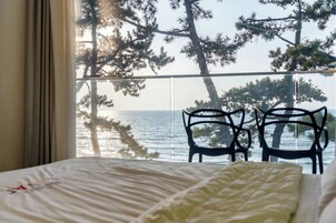 Una habitación con una cama, dos sillas y vistas al mar a través de una ventana.