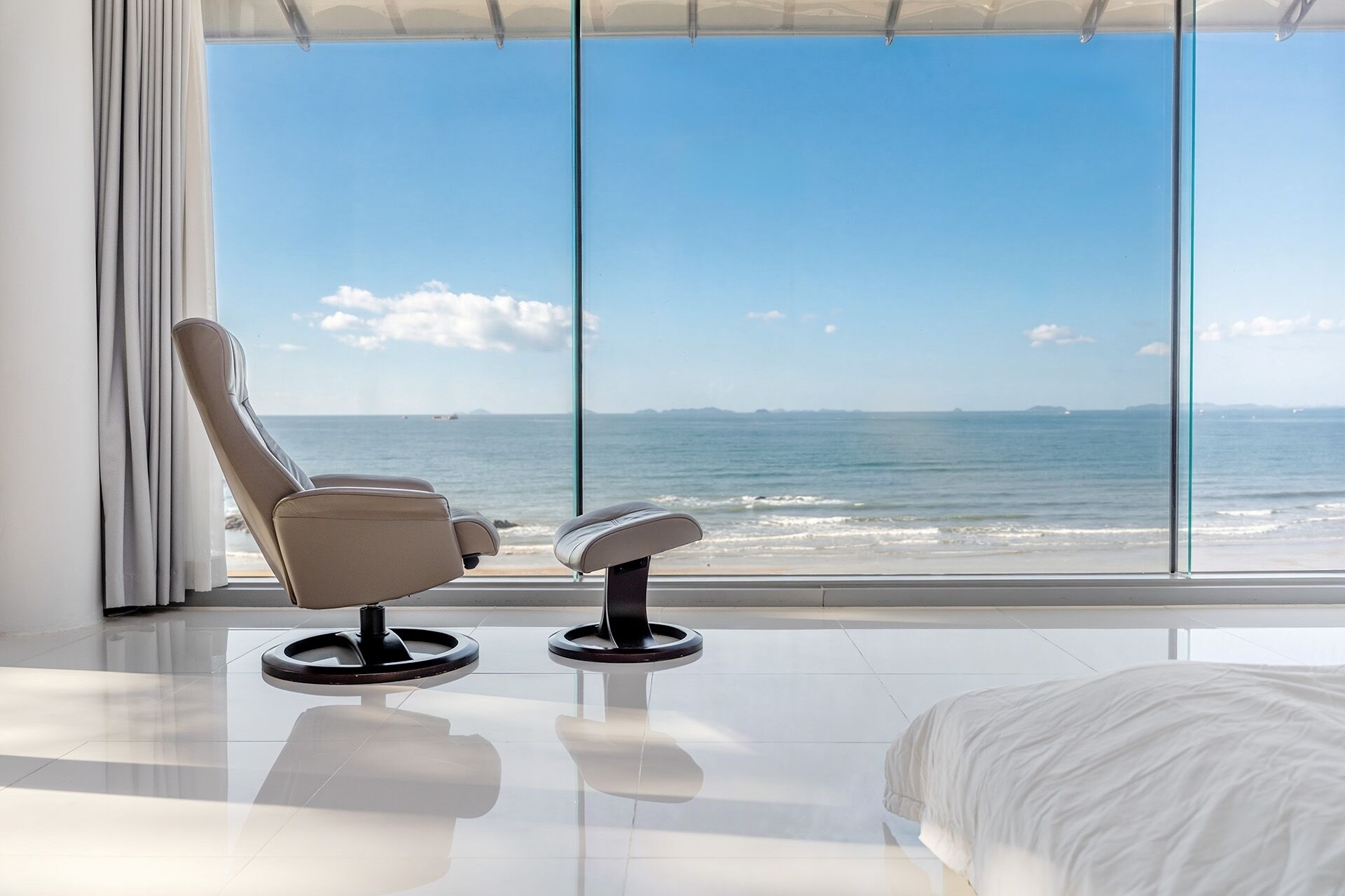 Ein modernes Zimmer mit großem Fenster mit Meerblick, einem weißen Bett und zwei Stühlen.