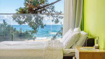 A hotel room with a bed, a nightstand, a lamp, and a view of the ocean.