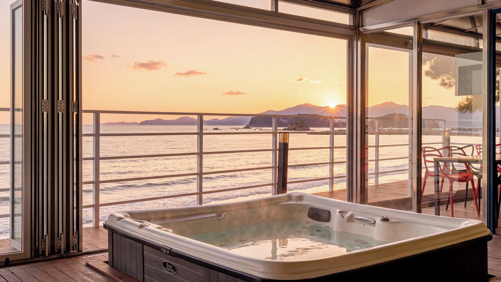 A hot tub on a wooden deck with a view of the ocean and mountains at sunset.