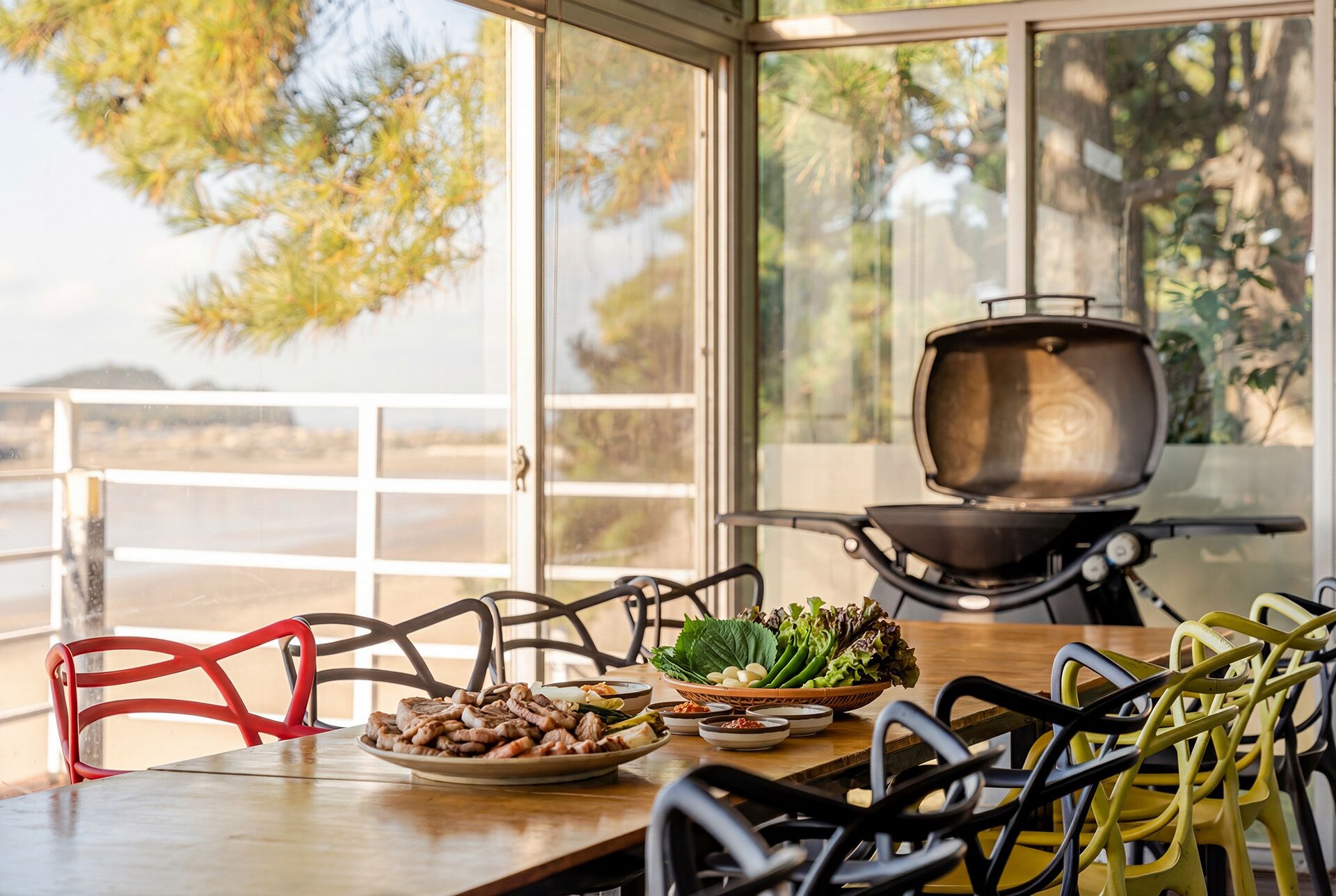A dining area with a table set for two, a grill, and a view of the outdoors.