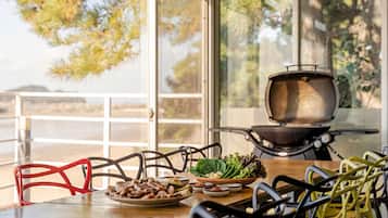 A dining area with a table set for two, a grill, and a view of the outdoors.