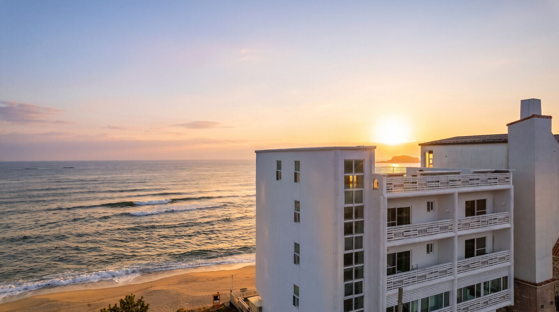 A coastal building with multiple balconies overlooking the ocean at sunset.