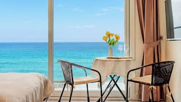 Una stanza con un'ampia finestra vista mare, un tavolo con un vaso di fiori gialli e due sedie.