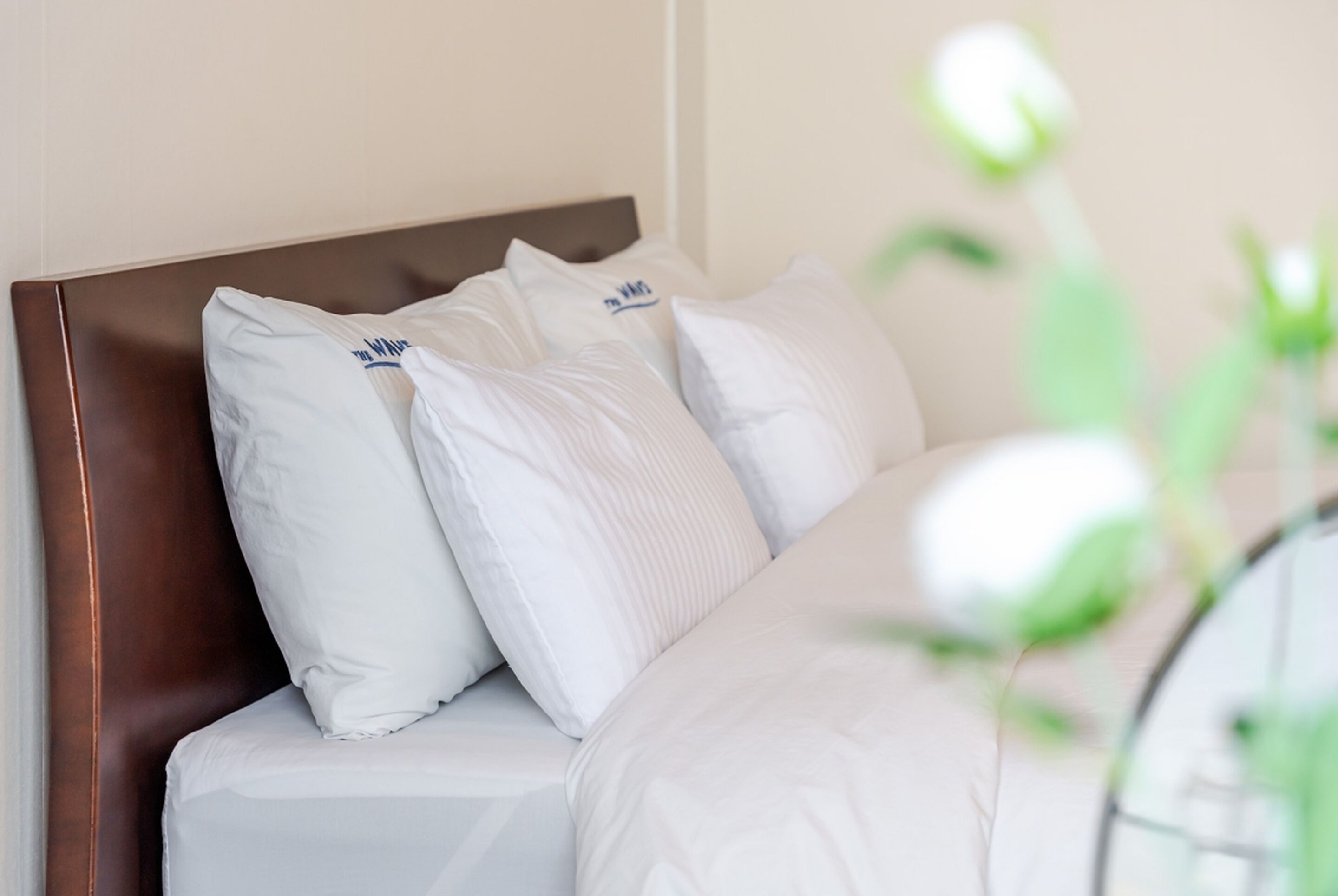 Cama bem arrumada com roupa de cama branca e cabeceira marrom.