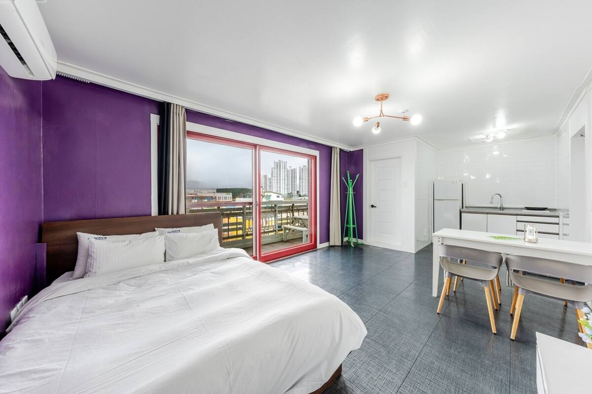 A modern hotel room with a large bed, a dining area, and a balcony with a city view.