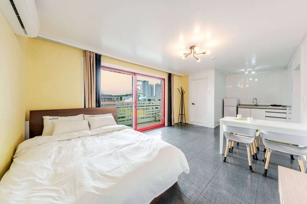 A hotel room with a bed, a desk, and a view of the cityscape through a large window.